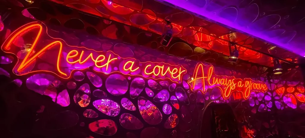 Neon sign "Never a cover Always a groove" on a purple reflective wall.