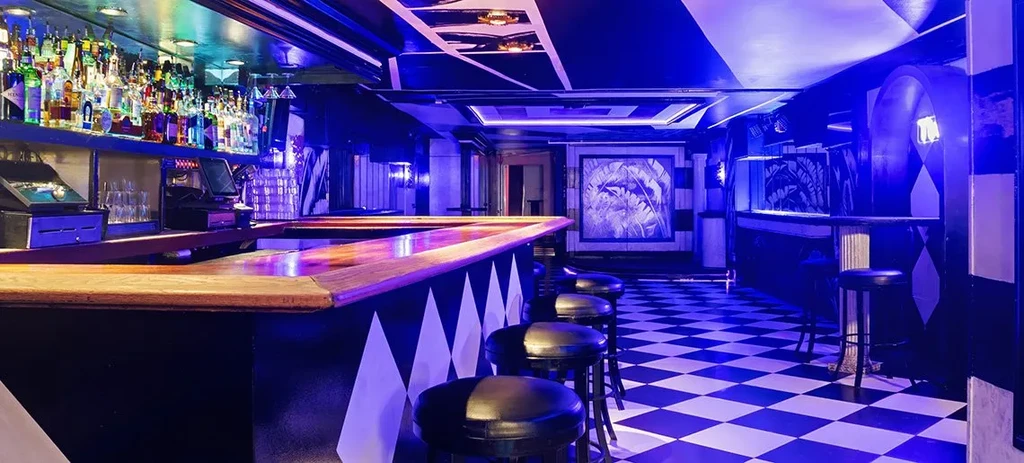 Empty modern bar interior with blue-lit liquor shelves and checkerboard floor.