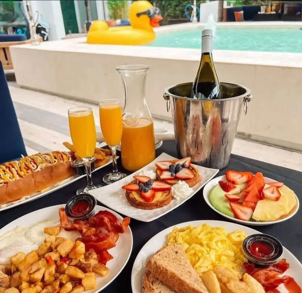 Outdoor brunch spread with hotdog, French toast, mimosas, by a pool.