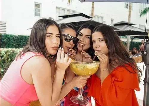 Four women outdoors sharing a giant fruit cocktail with straws.