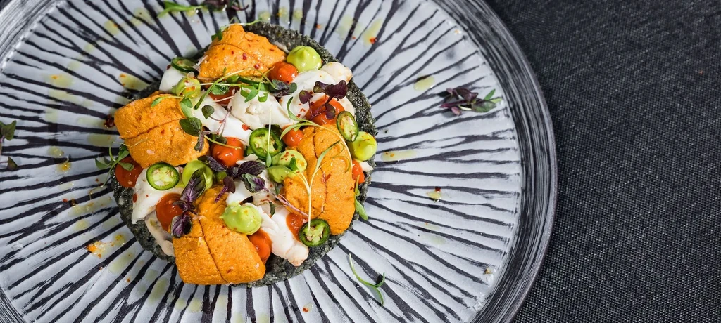 Artfully plated uni, white seafood, and vegetables on a striped plate.