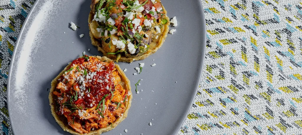 Two brightly colored sopes or tostadas topped with vegetables and meat.