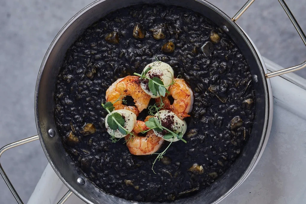 Black squid ink rice with four perfectly cooked, garnished shrimp.