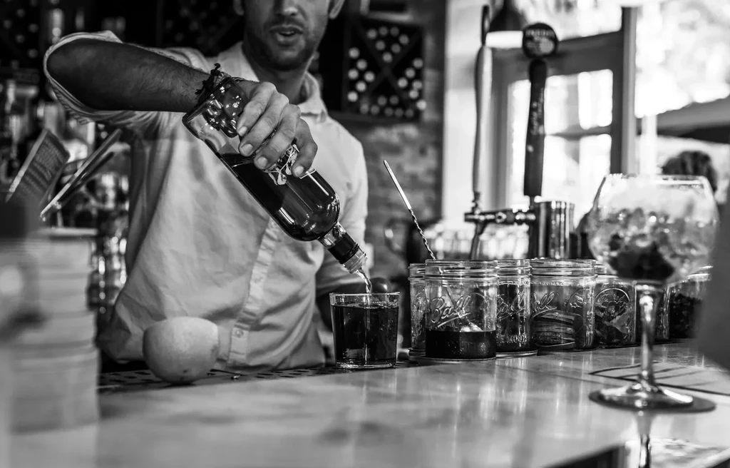 Bartender pouring a drink at a bar with mason jars visible.