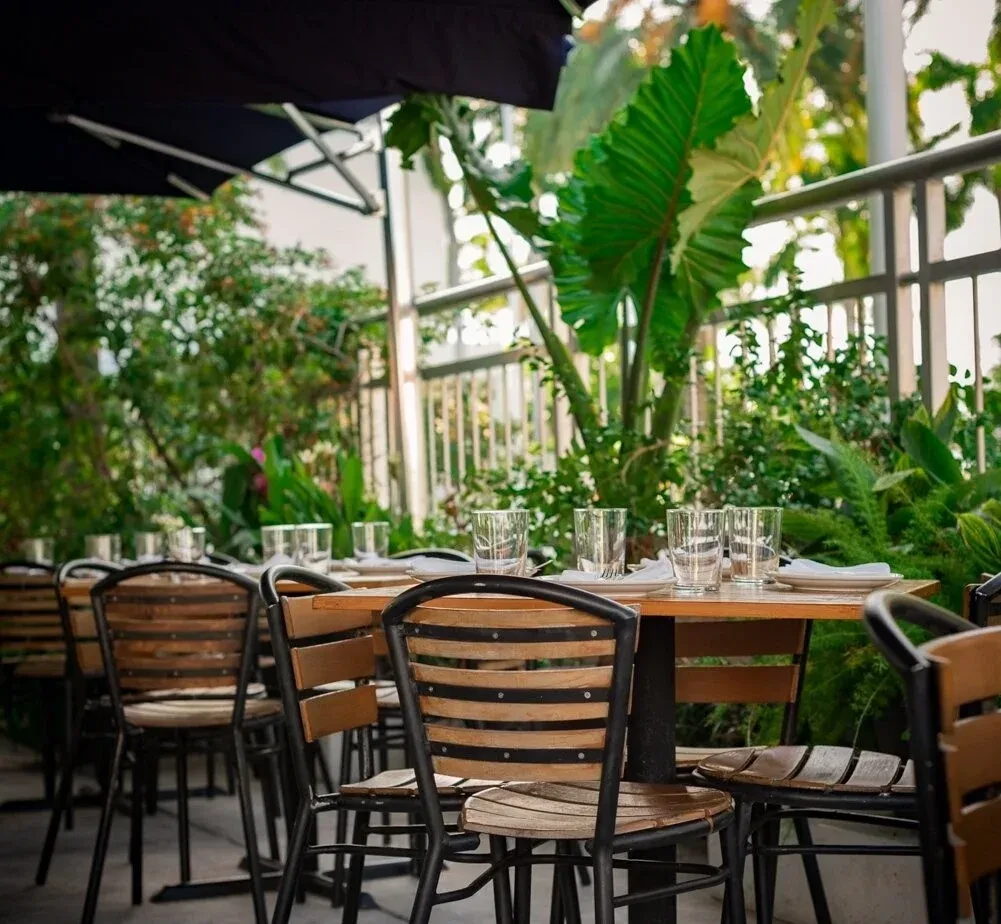 Outdoor patio with set wooden tables, chairs, and lush greenery.