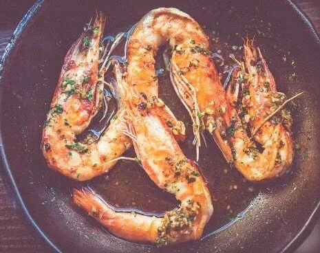 Roasted shrimp with herbs and garlic in a dark cast-iron pan.