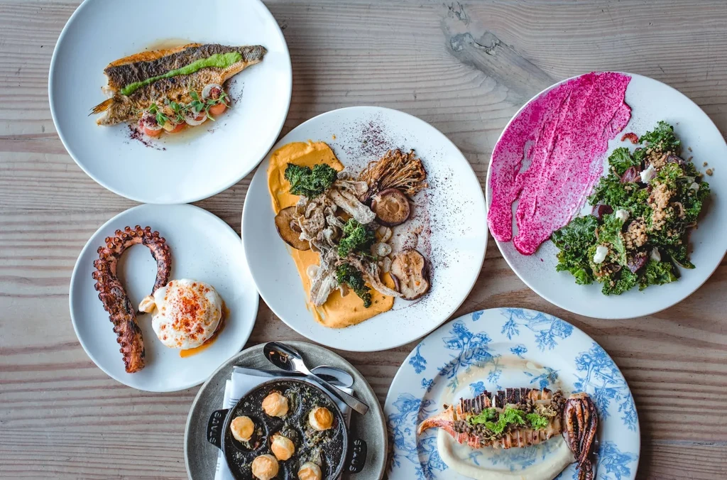 Overhead shot of six distinct, elegantly plated dishes on a wooden table.
