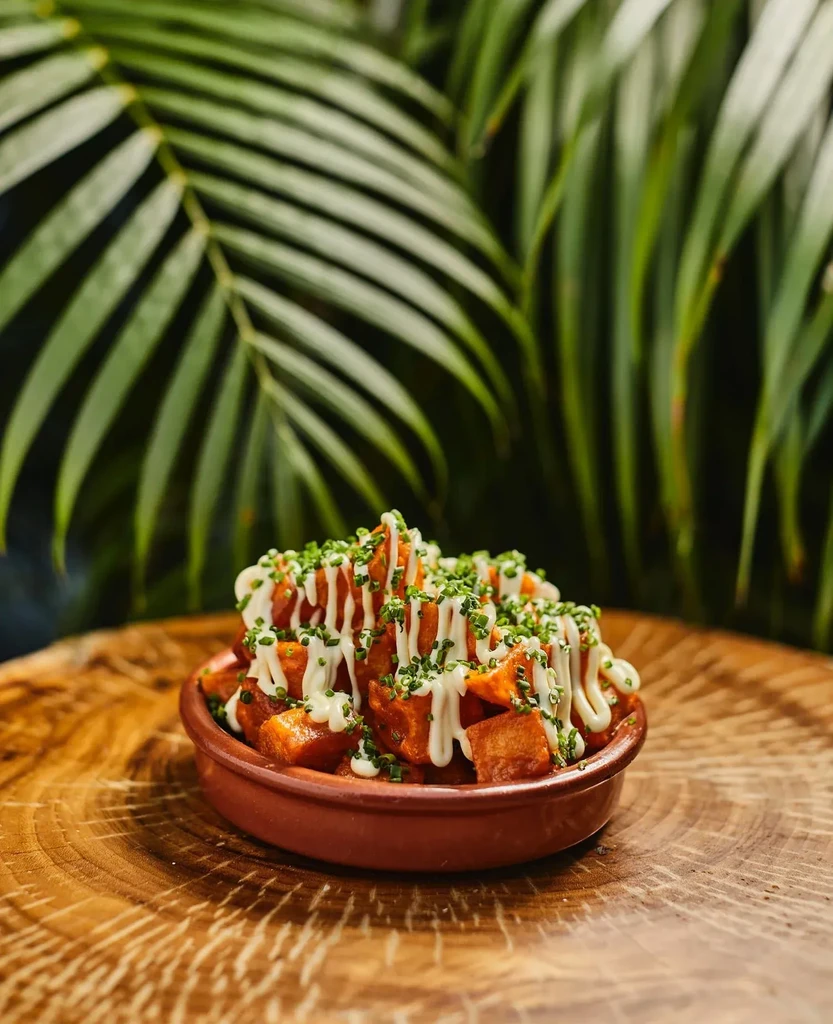 Rustic bowl of potato cubes with white sauce and green herbs.
