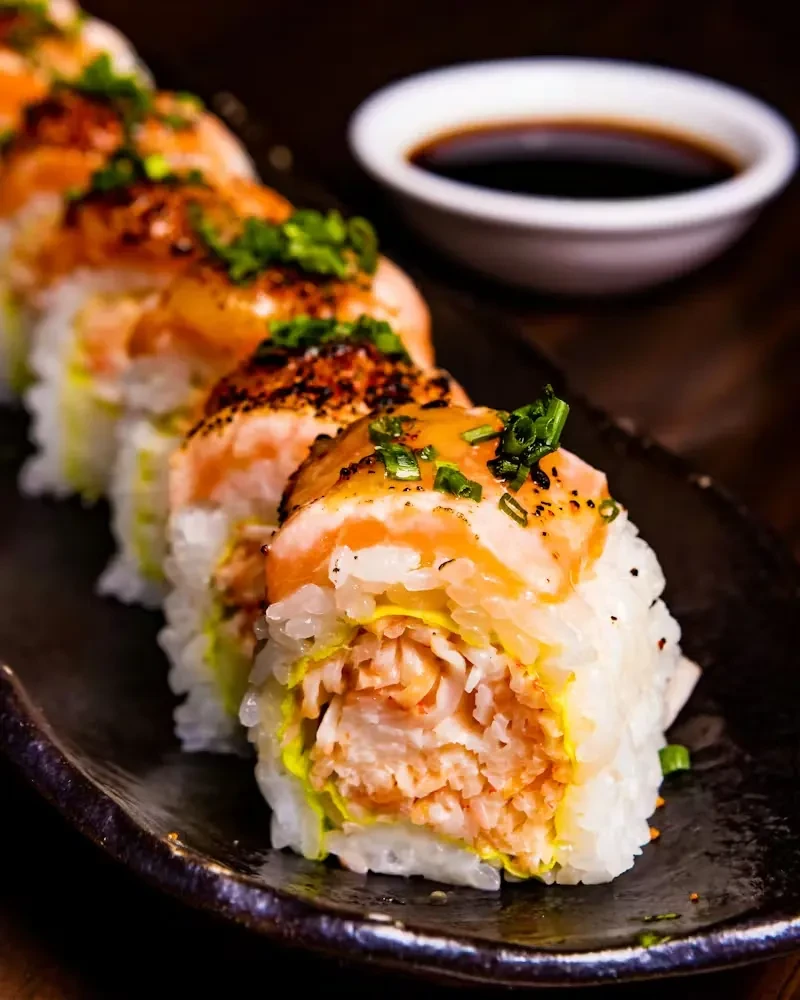 Six sushi rolls topped with seared salmon and green onions.