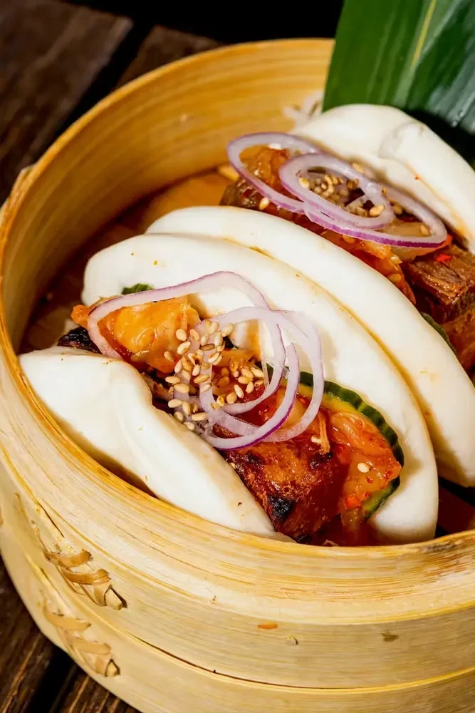Steamed bao buns filled with meat, cucumber, and kimchi in a steamer.