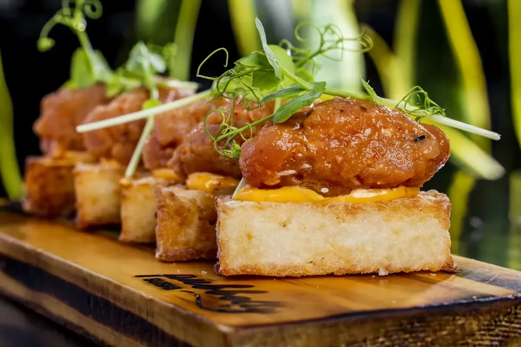 Fried chicken appetizers with spicy glaze and microgreens on a wooden board.