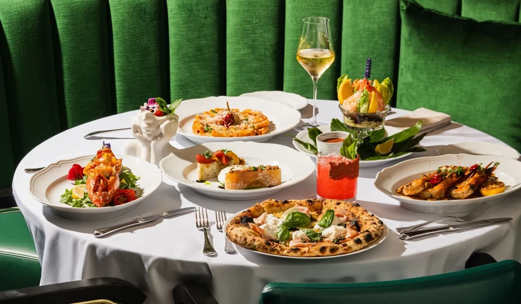 Table laden with gourmet pizza, prawns, lobster, pasta, and cocktails.