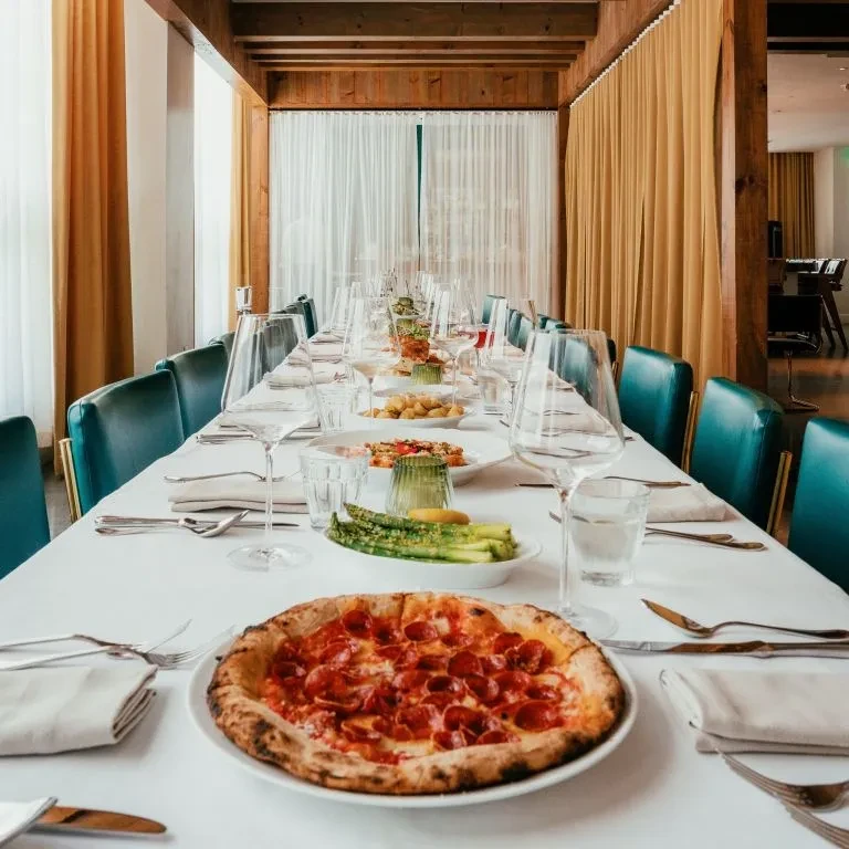 Long dining table set with pizza, asparagus, and appetizers in a restaurant.