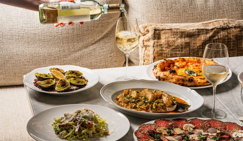 Hand pouring white wine amidst a spread of gourmet dishes.