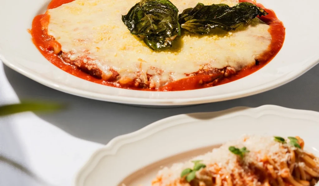 Close-up of baked pasta with melted cheese and basil, spaghetti blurred.