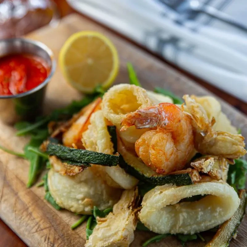 Fried shrimp, calamari, and vegetables with sauce on rustic board.