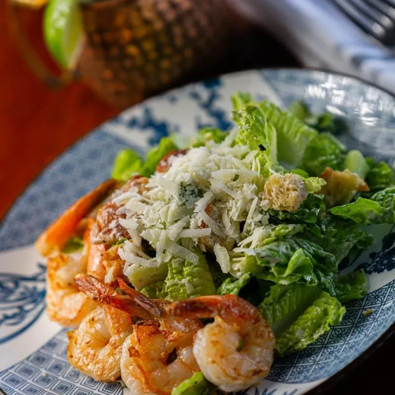 Caesar salad topped with grilled shrimp on a decorative blue and white plate.