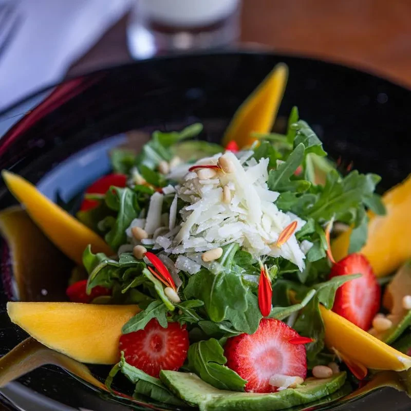 Colorful arugula salad with cheese, strawberries, avocado, and mango.