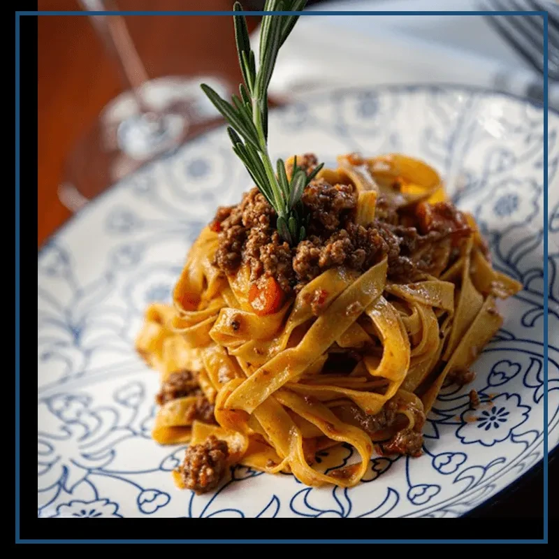 Tagliatelle pasta with Bolognese sauce, rosemary, on blue floral plate.
