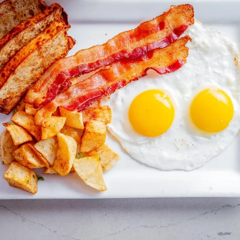 Overhead view of a breakfast plate with eggs, bacon, potatoes, and toast.