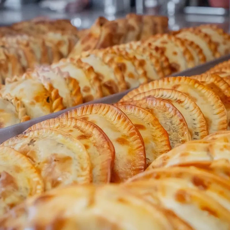 Rows of golden-brown empanadas or turnovers with crimped edges in trays.
