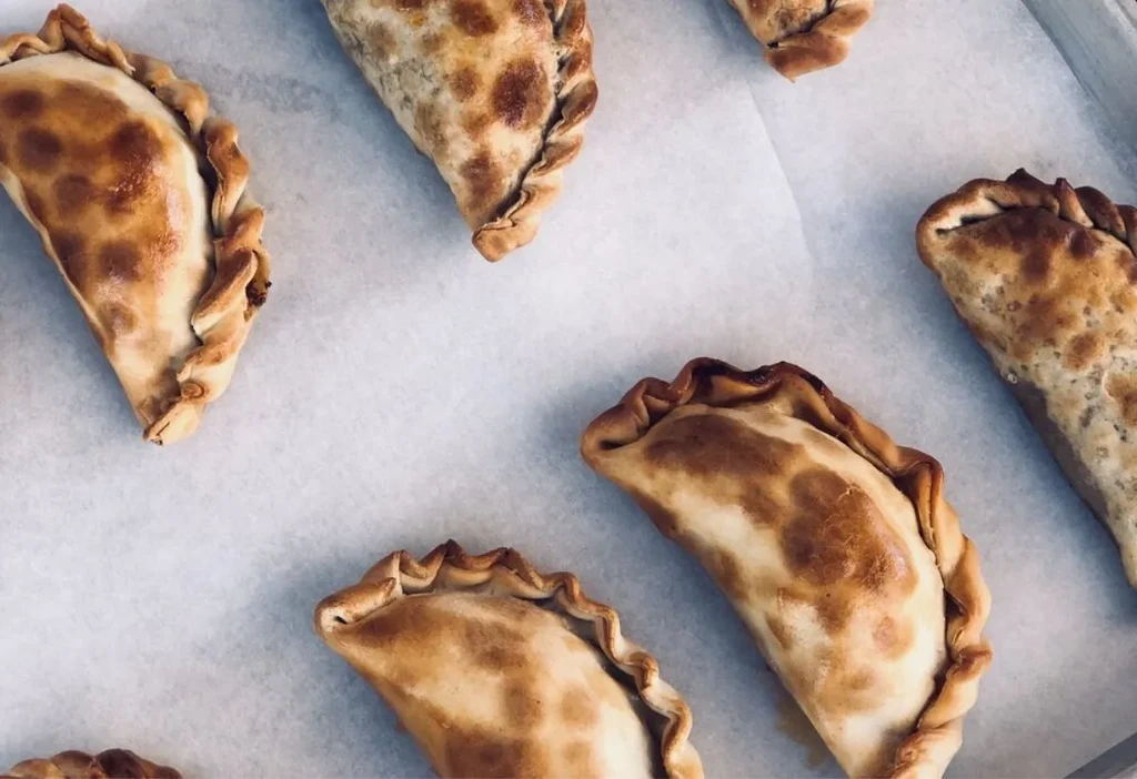 Multiple freshly baked golden-brown empanadas with crimped edges.