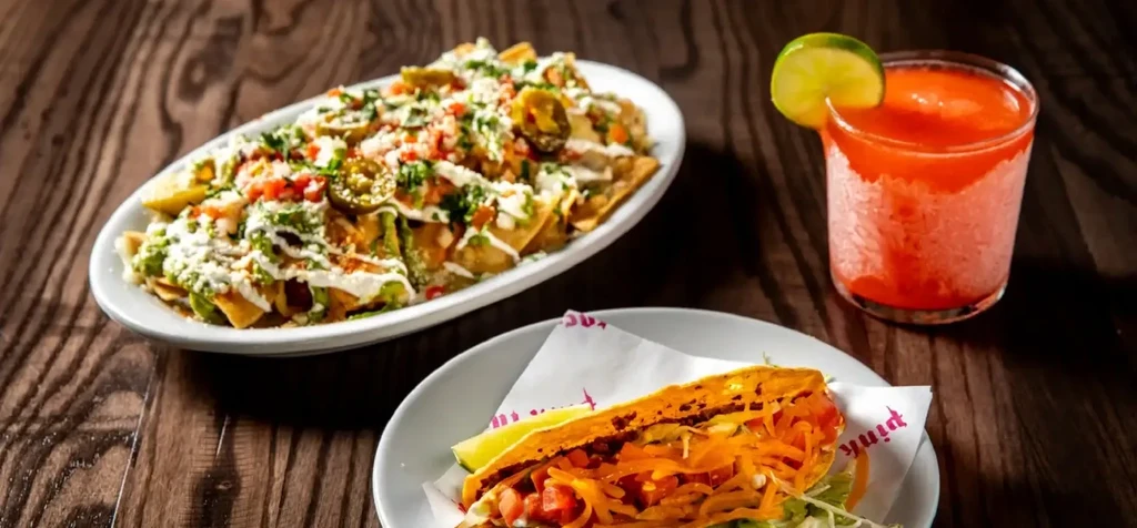 Loaded nachos, taco, and red frozen drink on a dark wooden table.