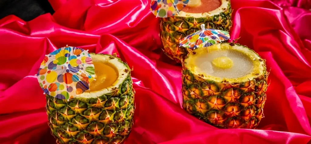 Three tropical pineapple drinks with umbrellas on pink satin.