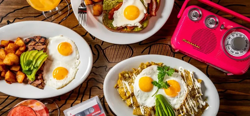 Overhead: Vibrant brunch dishes, fuchsia radio, and cassette on rustic wood.