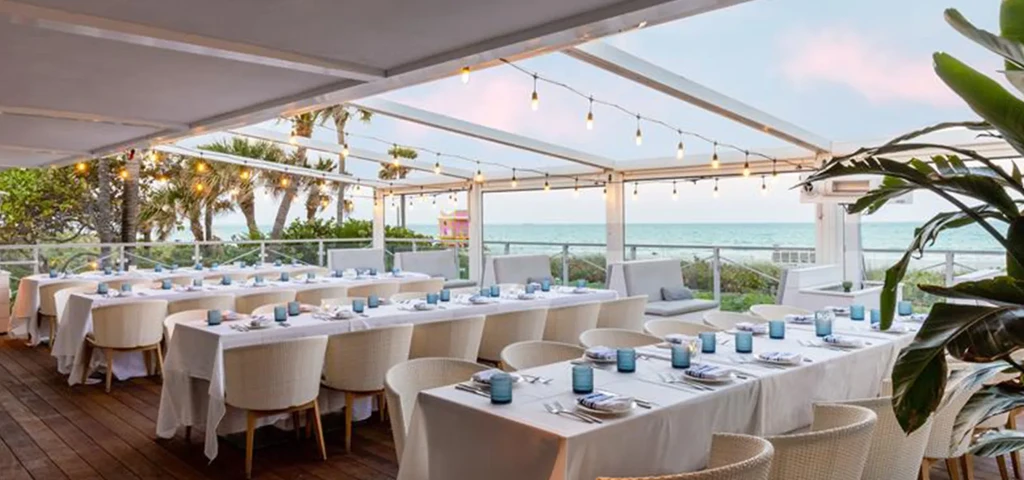 Meticulously set outdoor dining tables under lights, overlooking the ocean.