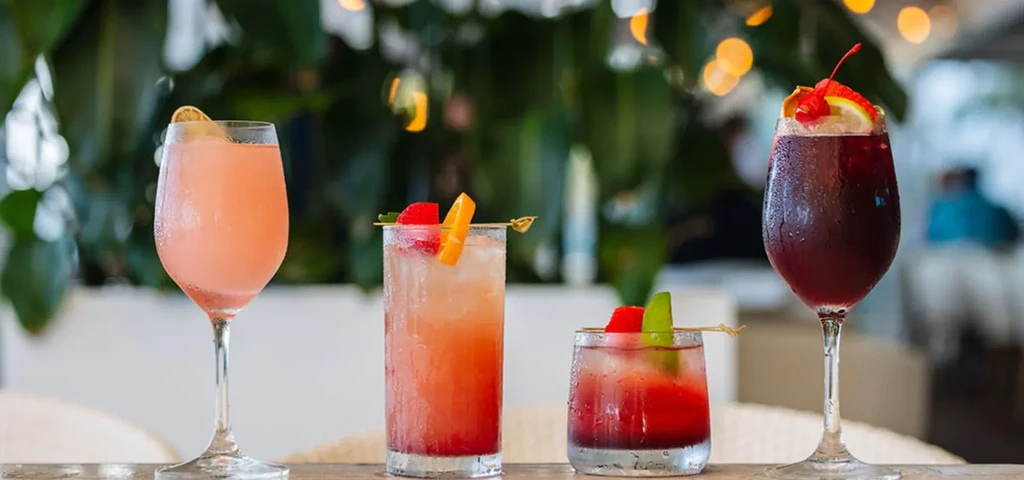 Close-up of four vibrant, garnished cocktails on a rustic wooden table.