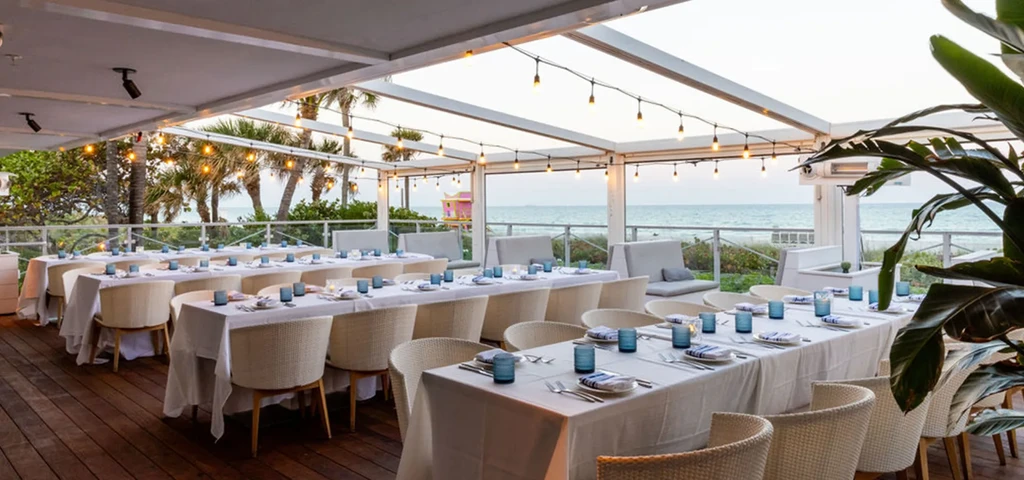Tropical beachfront restaurant patio with neatly set tables and string lights.