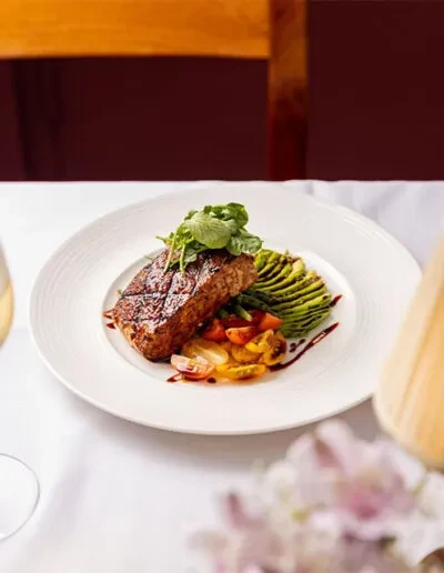 Plated grilled steak with avocado, tomatoes, greens, and balsamic drizzle.