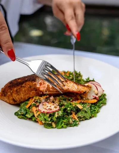 Hands with red nail polish cutting salmon and green salad.