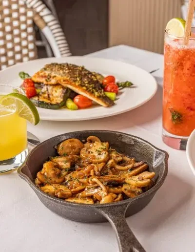 Pan-seared fish, sautéed mushrooms, and colorful drinks on a dining table.