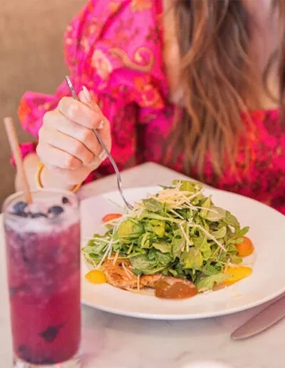 Close-up of person's hand eating a fresh salad and berry drink.