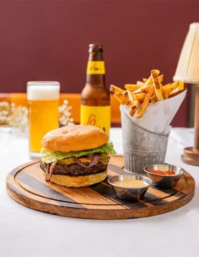 Gourmet burger on wooden board with fries in bucket and beer.