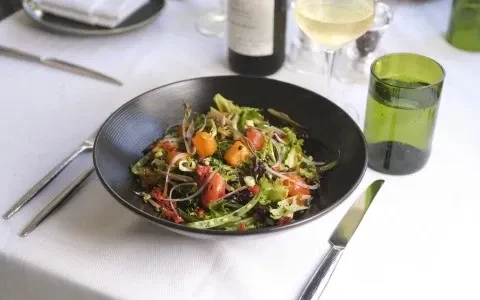 Close-up of a colorful salad, wine, and water on a white tablecloth.