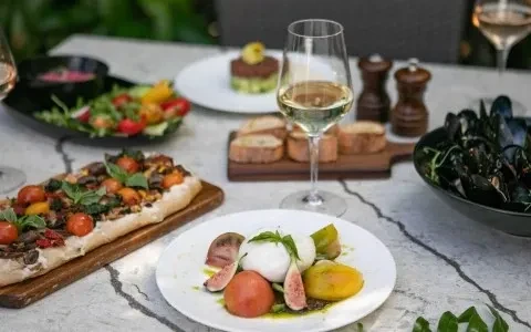 Outdoor table with burrata salad, flatbread, mussels, and white wine.