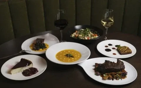 Six gourmet dishes and two wine glasses on a dark table.