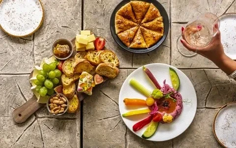 Overhead view of rustic table with charcuterie, crudités, flatbread, and wine.