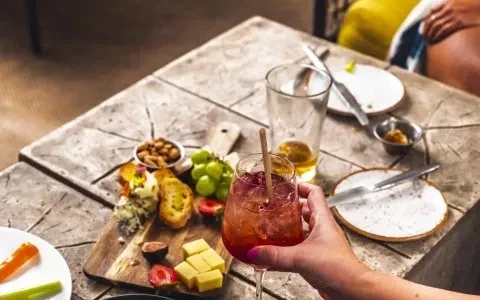 Overhead view of charcuterie board, vegetables, hand holding cocktail.