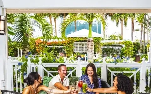 Four people toasting with drinks at a lush outdoor tropical restaurant.