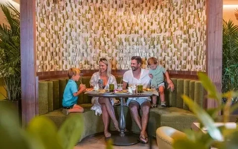 Happy family of four eating in a vibrant green restaurant booth.