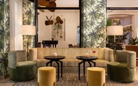 Opulent lounge with tufted sofa, cocktails, and palm tree patterned walls.