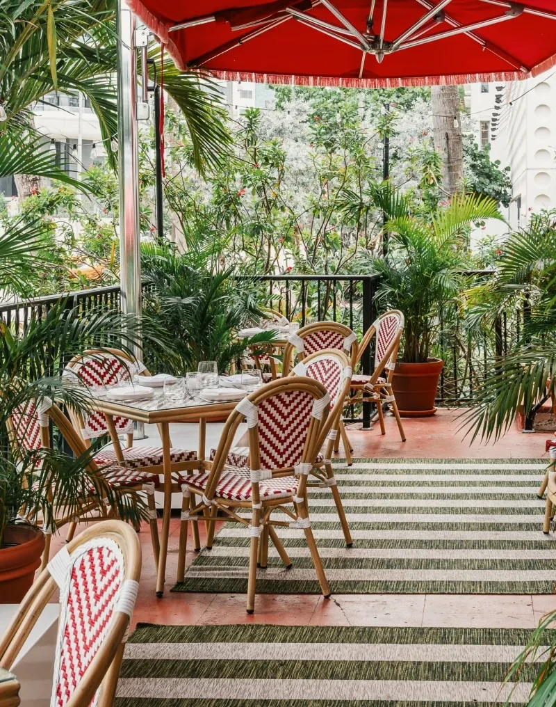 Terracotta patio with red umbrella, chevron chairs, tropical plants.