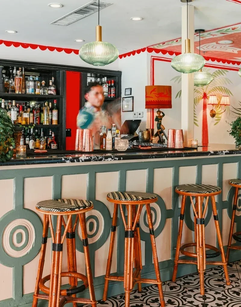 Lively bar with green paneled counter, geometric floor, and palm tree walls.