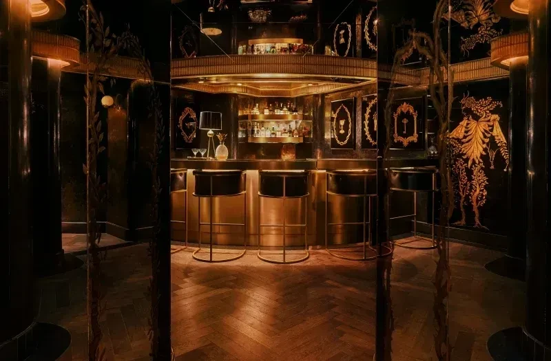 Dimly lit bar with golden counter, dark stools, and ornate gold walls.