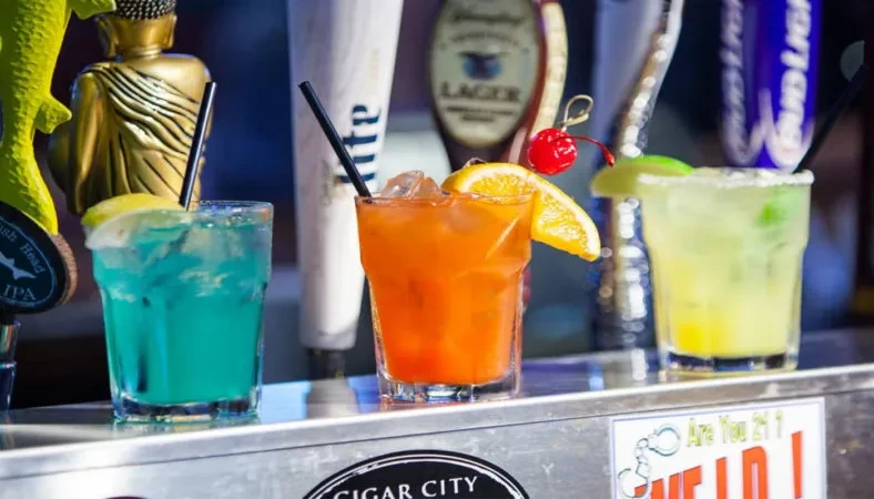 Three colorful cocktails on a bar counter with blurred beer taps.