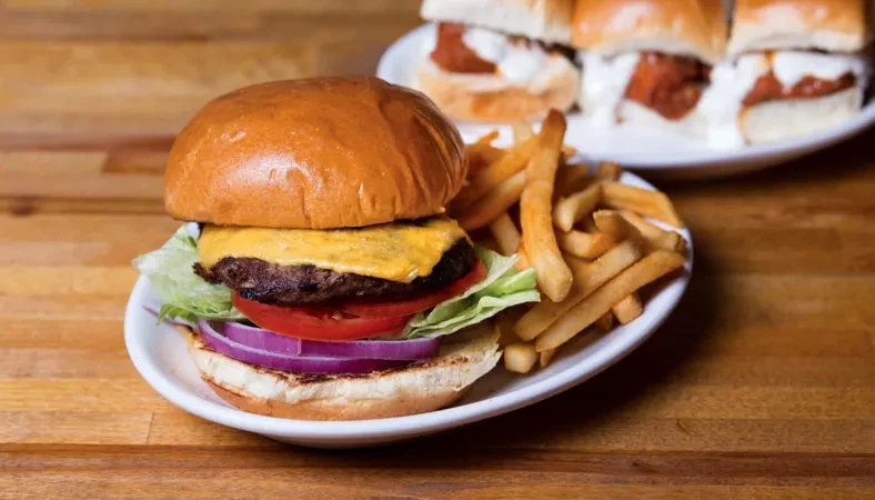 Close-up of a cheeseburger, fries, and sliders on a wooden table.